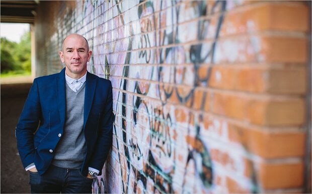 Jonathan Morgan, Partner at Zenko City Living, is pictured alongside a wall daubed with brightly coloured graffiti.