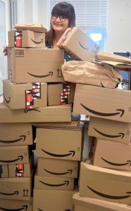 Location Location Operations Director Megan Eighteen is pictured in the office behind a stack of Amazon boxes reaching up to her neck.