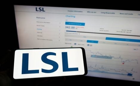 A mobile phone with LSL letters in front of a computer screen showing stock value.