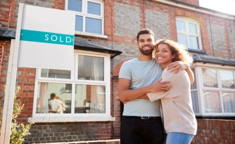 An excited heterosexual couple are pictured outside their first home which is a terraced house in England.