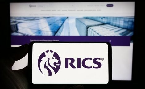 A mobile phone is pictured lengthways displaying the RICS logo in front of a laptop screen showing the RICS website.